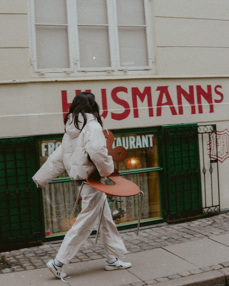 Connie's friend walking down the street while holding the chair.